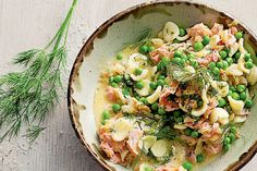 a bowl filled with pasta and peas on top of a wooden table next to a sprig of dill