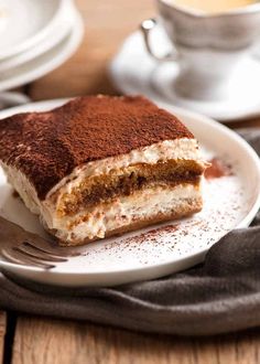 a piece of cake sitting on top of a white plate next to a cup of coffee