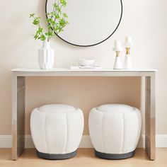 two white stools sitting under a round mirror on top of a wooden table next to a plant