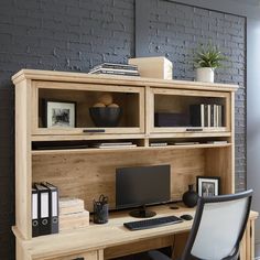 an office desk with a computer on it and bookshelf in front of the window