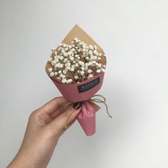 a hand holding a pink paper wrapped bouquet with white and brown flowers in it's wrapper