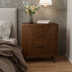 a bedroom with a bed, nightstand and flower vase on the night stand in front of it