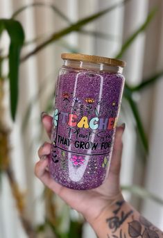 a person holding up a purple glittered tumbler with writing on the side and words that read teach, i don't grow food