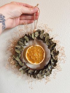 a hand holding a dried orange on top of a wreath with pine cones and leaves