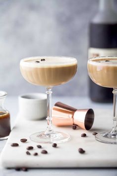 two glasses filled with drinks sitting on top of a white counter next to coffee beans