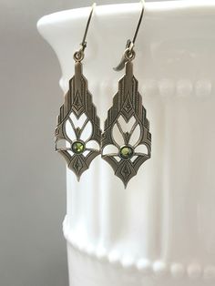 These modern Deco earrings are a great example of classic 1920s style. They feature ornate Art Deco style brass pendants. The pendants have a tiny olivine green crystal at the center These elegant earrings measure 2 inches long from the top of the ear wires to the bottom of the pendants. I love the simplicity of these Art Deco inspired earrings; perfect for everyday or evening. ABOUT THIS COLLECTION What are the three style essentials Jazz Age flappers like Clara Bow, Louise Brooks, and Zelda Fi Classic Pierced Chandelier Earrings For Formal Occasions, Classic Formal Chandelier Earrings With Intricate Design, Classic Brass Jewelry For Party, Silver Art Nouveau Jewelry For Evening, Ornate Chandelier Earrings For Formal Occasions, Art Deco Pierced Jewelry For Anniversary, Art Deco Filigree Jewelry For Evening, Art Deco Drop Earrings For Anniversary, Antique Bronze Earrings For Wedding