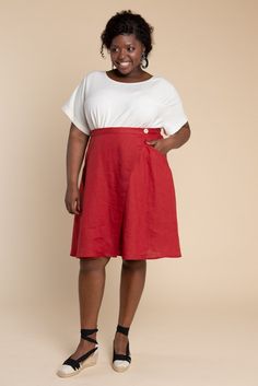 a woman standing in front of a beige background wearing a white t - shirt and red skirt