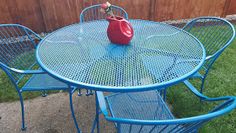 an outdoor table and chairs with a red vase on the top, in front of a wooden fence