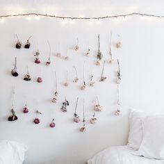 a white bedroom with flowers hanging on the wall and string lights above it, along with a bed