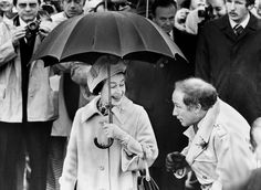 an old black and white photo of two people under an umbrella in front of a crowd