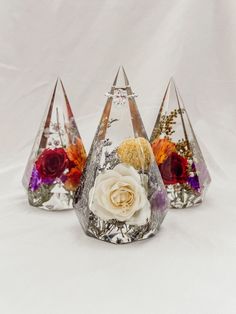 three glass vases with flowers in them on a white surface, one is upside down and the other two are upside down