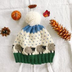 a knitted hat sitting on top of a table next to pine cones and an orange