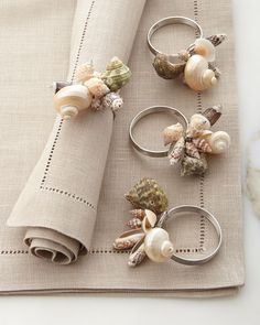 napkin rings with seashells on them are sitting on a place mat next to a folded napkin