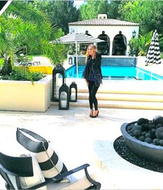 a woman standing in front of a pool next to lounge chairs and an umbrella on the patio