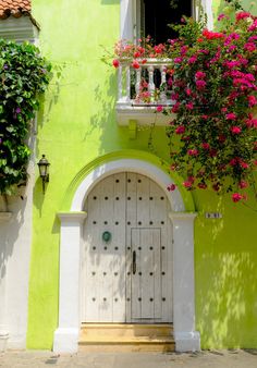 a green building with white doors and pink flowers on the windows sill above it