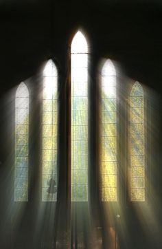 sunlight streaming through three stained glass windows in a church with green border around the edges