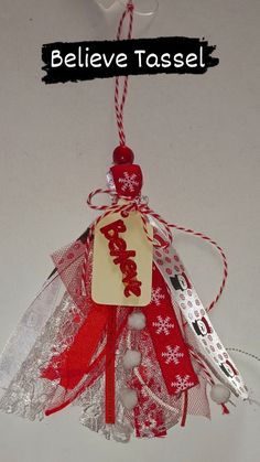 a red and white ornament hanging from a string with a tag that says believe tassel