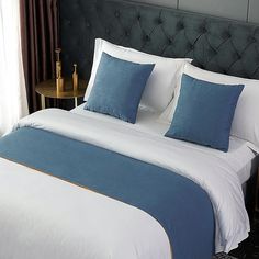 a bed with blue and white pillows in a bedroom next to a night stand that has a lamp on it