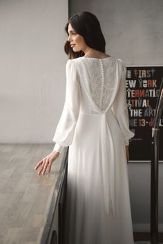 a woman in a white dress is standing near a railing and looking at the wall