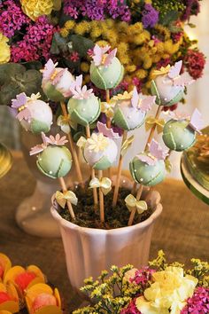 there are many flowers in the vase and some cake pops on the table with them