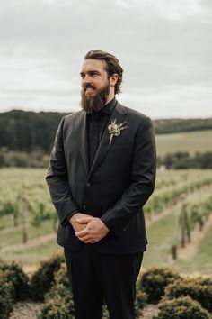 a man with a beard wearing a black suit and flower in his lapel is looking at the camera