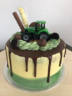 a green and yellow cake with a tractor on top that has chocolate drizzle