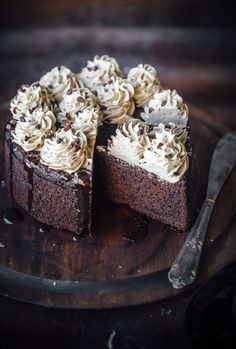 a chocolate cake with white frosting and sprinkles on top sits on a wooden platter