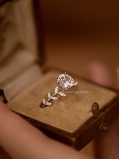 a close up of a person holding a ring in a box with a flower on it