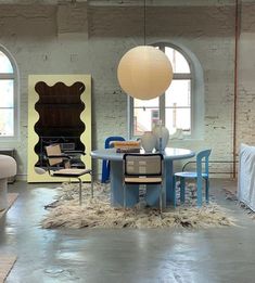 a living room filled with lots of furniture next to two large windows and a round table surrounded by chairs