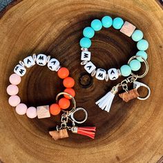 two bracelets with charms and tassels are on a wooden surface next to a piece of wood