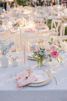 the table is set with pink and white flowers in vases, plates and napkins