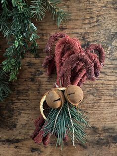 two bells on top of a wooden table next to pine needles and evergreen branches with red cloth