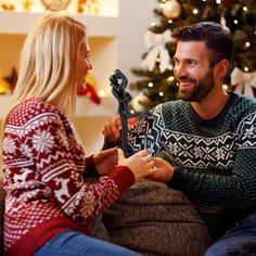 a man and woman sitting on a couch in front of a christmas tree talking to each other