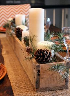 a wooden box filled with candles and pine cones on top of a dining room table