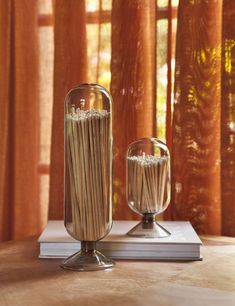 two glass vases filled with noodles on top of a table next to a window