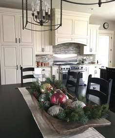 a dining room table decorated for christmas with ornaments and greenery on the centerpiece