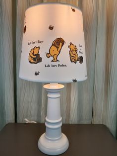 a lamp with winnie the pooh on it sitting on a table next to curtains