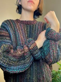 a woman wearing a multicolored sweater and holding her hands on her chest with one hand