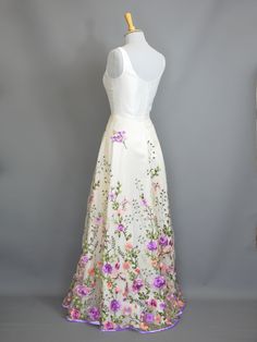 a dress on a mannequin with flowers all over it and purple trim around the waist