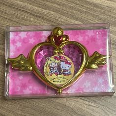 a gold heart shaped brooch sitting on top of a wooden table next to a pink box