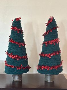 two christmas trees made out of crocheted yarn on top of a wooden table