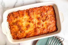 a casserole dish with cheese and meat in it sitting on a table next to a fork