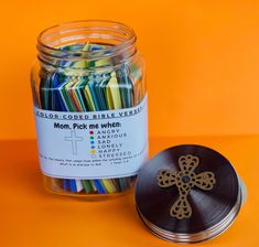 a glass jar filled with colored crayons next to a metal container on an orange surface