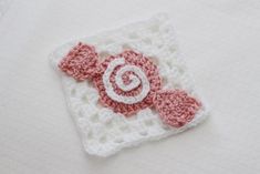 a crocheted square with a pink and white flower on it sitting on a table