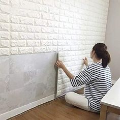 a woman is sitting on the floor painting a brick wall with white paint and tape