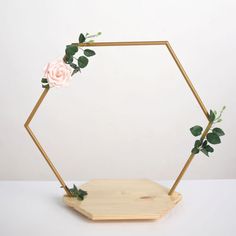 a wooden hexagonal frame with flowers and greenery around it on a white surface