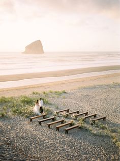 a bride and groom are standing on the beach