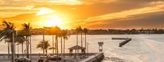 the sun is setting over the water and palm trees