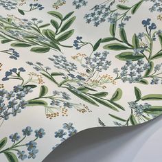 a white and blue flowered wallpaper with green leaves on the top, along with small blue flowers