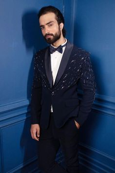 a man in a tuxedo standing against a blue wall